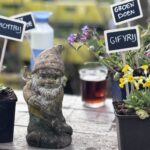 Beschermkabouter van onze kwekerij tussen potplantjes met bordjes 'dichtbij', 'gifvrij' en 'groen doen'